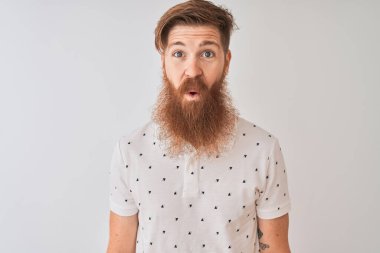 Genç kızıl saçlı, polo giyen, yalnız beyaz arka planda duran, korkmuş ve şok olmuş bir adam..