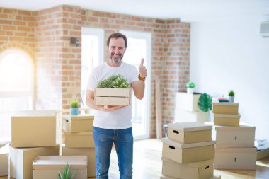 Orta yaşlı bir adam yeni evine taşınıyor. Karton kutuları paketliyor. Kocaman gülümsüyor.