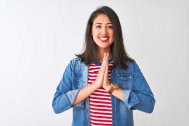 İzole edilmiş beyaz arka plan üzerinde çizgili tişört ve kot giyen genç Çinli kadın ellerini birleştirip af diliyor kendinden emin bir şekilde gülümsüyor.