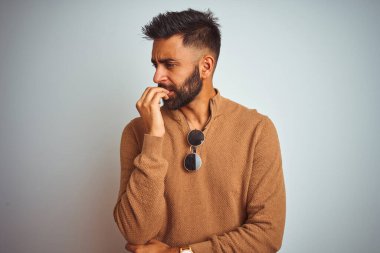 Zarif süveter ve güneş gözlüğü takan Hintli bir adam izole edilmiş beyaz arka plan üzerinde gergin ve gergin görünüyor. Endişe sorunu.