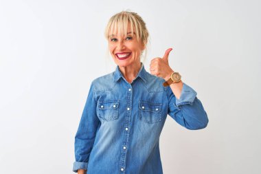 Orta yaşlı kadın, izole edilmiş beyaz arka planda dikilmiş sıradan bir kot gömlek giyiyor ve mutlu bir el hareketi yapıyor. Kameraya bakıp başarıyı gösteren ifade onaylanıyor.