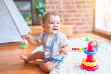 Anaokulunda battaniyeye oturmuş gülümseyen güzel bir bebek.