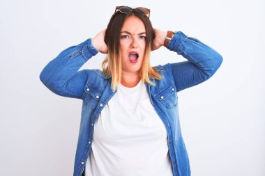 Güzel bir kadın kot gömlek giyer, beyaz arka planda durur. Deli ve korkmuş, elleri başında, korkmuş ve ağzı açık bir şekilde şok geçirmekten korkan.