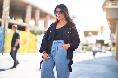 Güneş gözlüğü takan genç ve güzel bir kadın mutlu ve kendinden emin gülümsüyor. Şehir caddesinde ayakta ve yürüyorum.