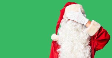 Orta yaşlı yakışıklı adam, Noel Baba kostümü ve sakal takıyor. Gülümsüyor ve gülümsüyor. Yüzünde şaşkınlık için gözleri örtüyor. Kör kavram.