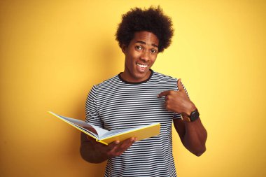 Afro-Amerikalı öğrenci kitap okuyor. İzole edilmiş sarı arka planda duruyor. Yüzü kendini işaret ediyor.