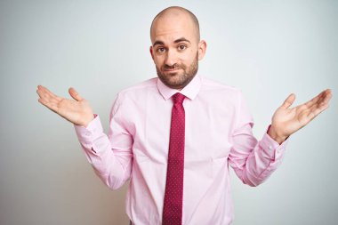 Pembe kravat takan genç iş adamı soyutlanmış arka plan bilgisiz ve elleri ve elleri havada kafası karışmış bir ifade takınıyor. Şüphe kavramı.