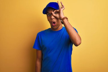 Yakışıklı Arap teslimatçı, izole edilmiş sarı arka planda duruyor. Şaşırmış yüz ifadesiyle şaşırmış, parmaklarından bakan gözler. İnançsız ifade.