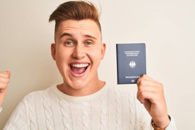 Genç yakışıklı adam Almanya pasaportunu izole edilmiş beyaz arka planda tutuyor gururla bağırıyor, zaferi ve başarıyı kutluyor çok heyecanlı, coşkulu bir duygu.