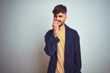 İzole edilmiş beyaz arka planda duran bornoz giyen genç adam elleri ağız yiyen tırnaklarla gergin ve stresli görünüyor. Endişe sorunu.