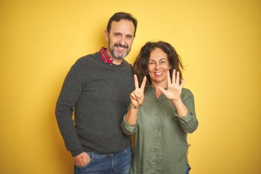 Güzel orta yaşlı çift, izole edilmiş sarı arka planda 7 numaralı parmaklarını gösterip gülümserken mutlu ve kendinden emin..