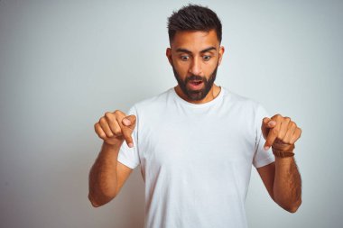 İzole edilmiş beyaz arka planda duran tişörtlü genç Hintli adam parmaklarını göstererek reklamını yapıyor, şaşırmış yüzünü ve ağzını açıyor.