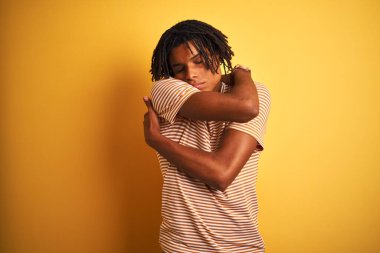 Rastalı tişörtlü Afro bir adam izole edilmiş sarı arka planda dikiliyor mutlu ve pozitif, kendinden emin gülümsüyor. Sevgi ve özgüven.