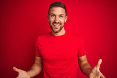 Kırmızı izole edilmiş arka plan üzerine gündelik tişört giyen yakışıklı genç adam güler yüzlü, kolları açık, dostça karşılama, olumlu ve kendinden emin selamlar.