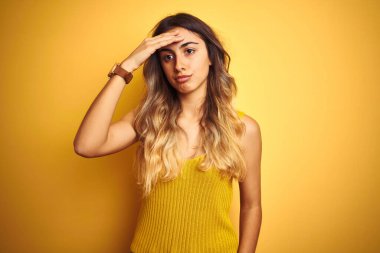 Sarı arka plan üzerine tişört giyen genç ve güzel bir kadın. Alnındaki bir sorun yüzünden endişeli ve stresli. Kriz için endişeli.