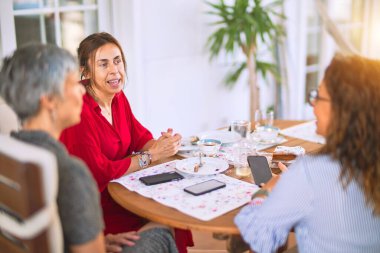 Orta yaşlı kadınlarla buluşup, öğle yemeği yiyip, kahve içiyorlar. Olgun arkadaşlar mutlu bir şekilde gülümsüyor. Güneşli bir günde evde akıllı telefon kullanıyorlar.