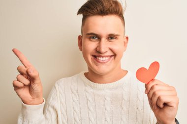 Genç, yakışıklı, romantik bir adam. Elinde kağıt kalpler var. İzole edilmiş beyaz arka planda duruyor.