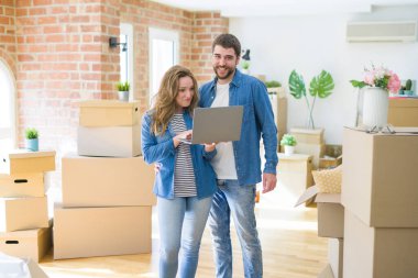 Yeni bir daireye taşımak için mutlu karton kutular etrafında bir odada bilgisayar laptop ayakta kullanarak genç çift