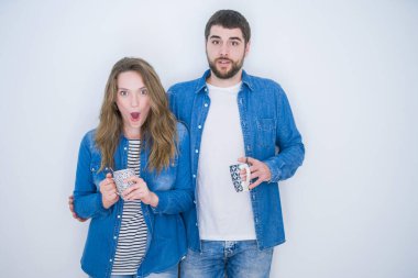 Genç ve güzel bir çift, beyaz izole edilmiş arka planda bir fincan kahve içiyorlar. Şaşırmış bir yüzle şoktan korkuyorlar ve korku ifadesinden korkuyorlar.