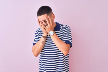 Pembe izole edilmiş arka plan üzerine deniz çizgili tişört giyen genç yakışıklı bir adam. Ağlarken suratını ellerle kapatan üzgün bir ifade. Depresyon kavramı.