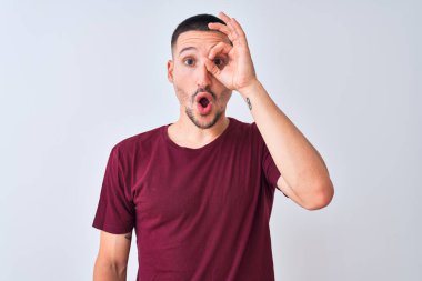 Soyutlanmış arka planda duran yakışıklı genç adam şaşırmış yüz ifadesiyle şaşırmış bir şekilde hareket ediyor ve parmaklarının arasından bakıyor. İnançsız ifade.