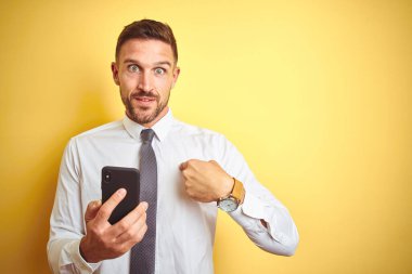Genç yakışıklı iş adamı, sarı izole edilmiş arka planda akıllı telefon kullanıyor.