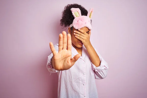 年轻的非洲裔美国女人 戴着睡衣 戴着面具 戴着孤立的粉色背景 用手捂住眼睛 用悲伤和恐惧的表情做着停止动作 尴尬和消极的概念 — 图库照片