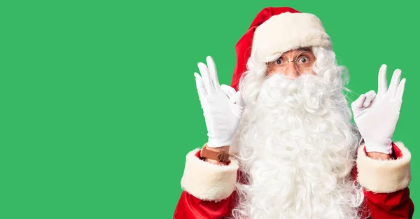 中年男子穿着圣诞老人的服装 蓄着胡子 站在那里惊讶地看着 用手指做着一个认可的标志 疯狂的表情 — 图库照片
