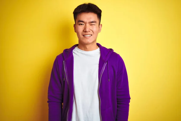 若いですアジアの中国人男性身に着けていますパープルスウェットシャツ立って上の隔離された黄色の背景ウィンク見ますザカメラとともにセクシー式 陽気で幸せな顔 — ストック写真