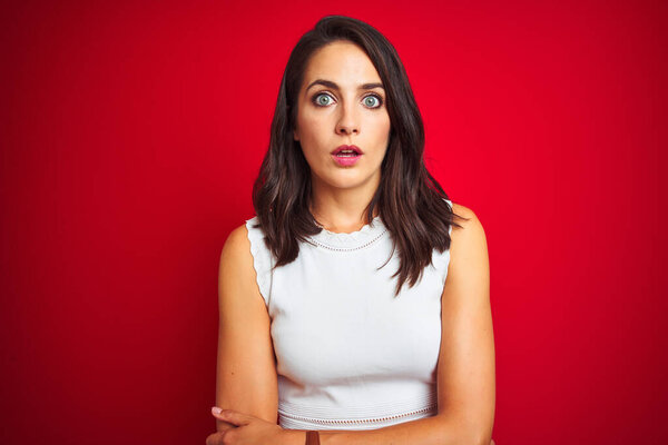 Young beautiful woman wearing white dress standing over red isolated background afraid and shocked with surprise expression, fear and excited face.