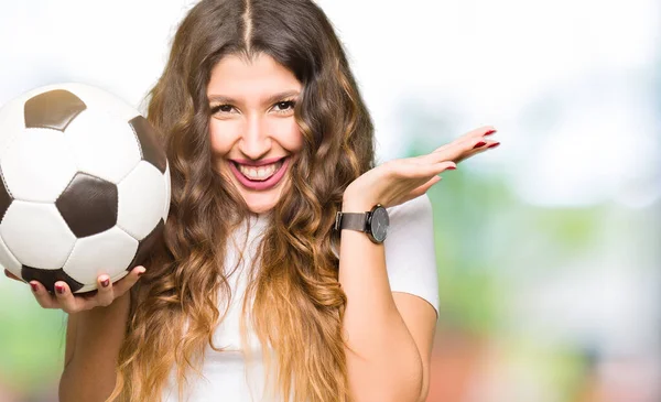 Young adult woman holding soccer football ball very happy and excited, winner expression celebrating victory screaming with big smile and raised hands