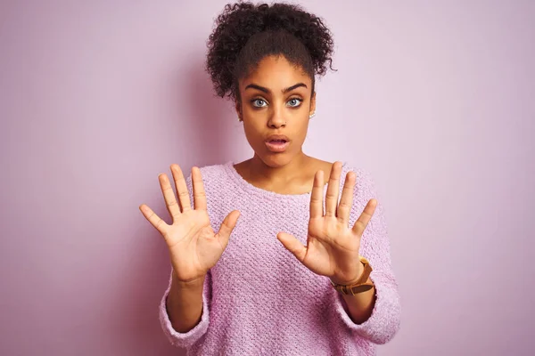 Young african american woman wearing winter sweater standing over isolated pink background Moving away hands palms showing refusal and denial with afraid and disgusting expression. Stop and forbidden.