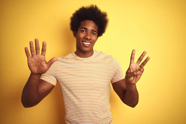 American man with afro hair wearing striped t-shirt standing over isolated yellow background showing and pointing up with fingers number eight while smiling confident and happy.