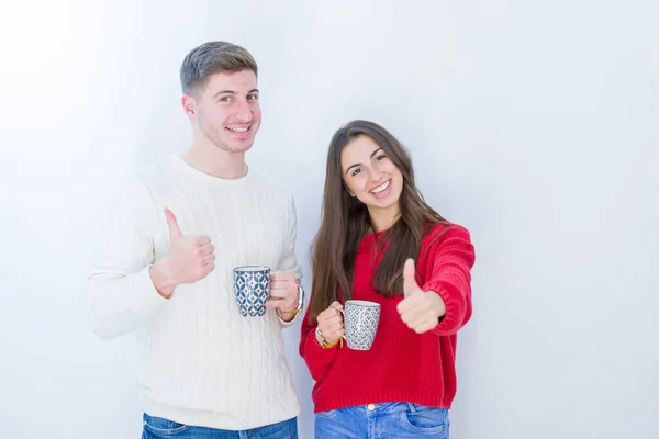 美丽的年轻夫妇在孤独的白色背景上喝着一杯咖啡 开心的笑着做个好手势 用手指竖起大拇指 很好的标志 — 图库照片