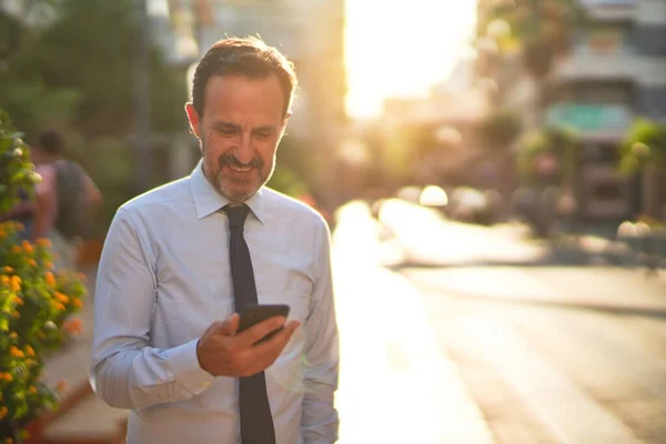 中年英俊商人在街上用智能手机微笑 — 图库照片