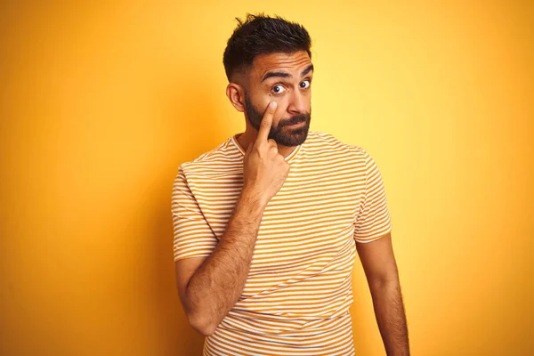 孤立した黄色の背景の上に立ってTシャツを着て若いインドの男あなたのジェスチャーを見て目を指す 疑わしい表現 — ストック写真