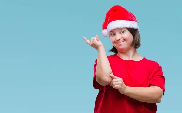 カメラを見て側に手と指で指しているダウン症の顔に大きな笑みを浮かべて隔離された背景にクリスマスの帽子をかぶっての若い大人の女性 — ストック写真