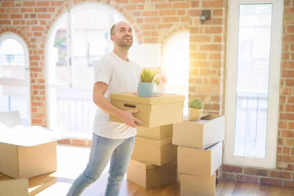 Joven hombre guapo mudándose a una casa nueva, sosteniendo cajas de cartón smil —  Fotos de Stock