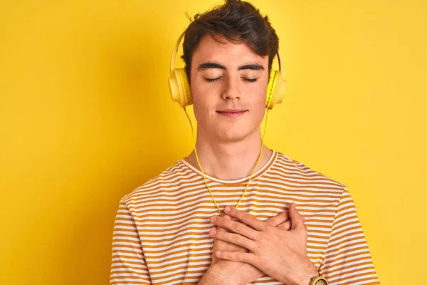 Teenager Boy Wearing Headphones Isolated Yellow Background Smiling Hands Chest — Stockfoto