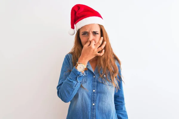 孤立した背景の上にクリスマスの帽子をかぶっている若い美しい赤毛の女性は 臭いと嫌な 耐えられない匂いを嗅ぎ 鼻に指で息をしています 悪い匂いの概念 — ストック写真