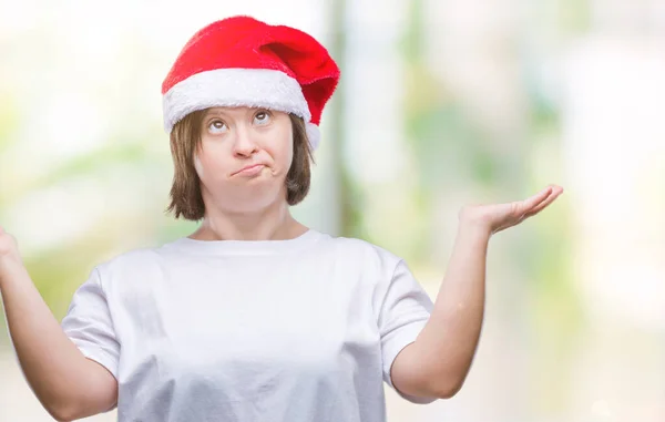 上クリスマス帽子をかぶっているダウン症候群の若い大人の女性は 腕と手を上げて背景無知と混乱して式を隔離しました 疑いのコンセプト — ストック写真