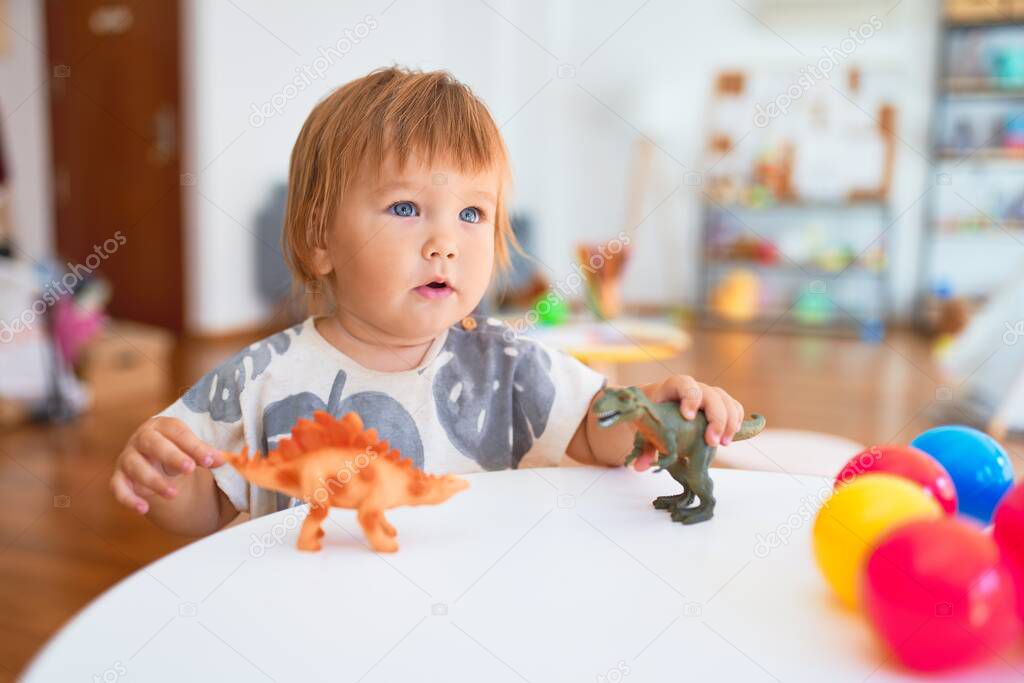 Adorable toddler playing with dinosaurs around lots of toys at kindergarten