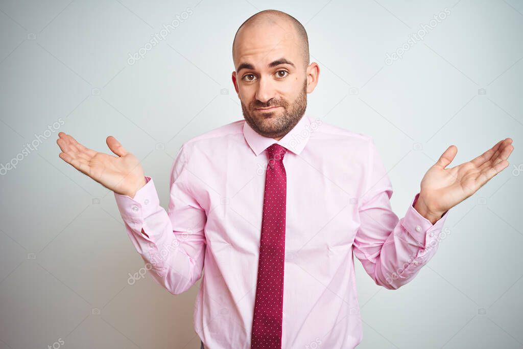 Young business man wearing pink tie over isolated background clueless and confused expression with arms and hands raised. Doubt concept.