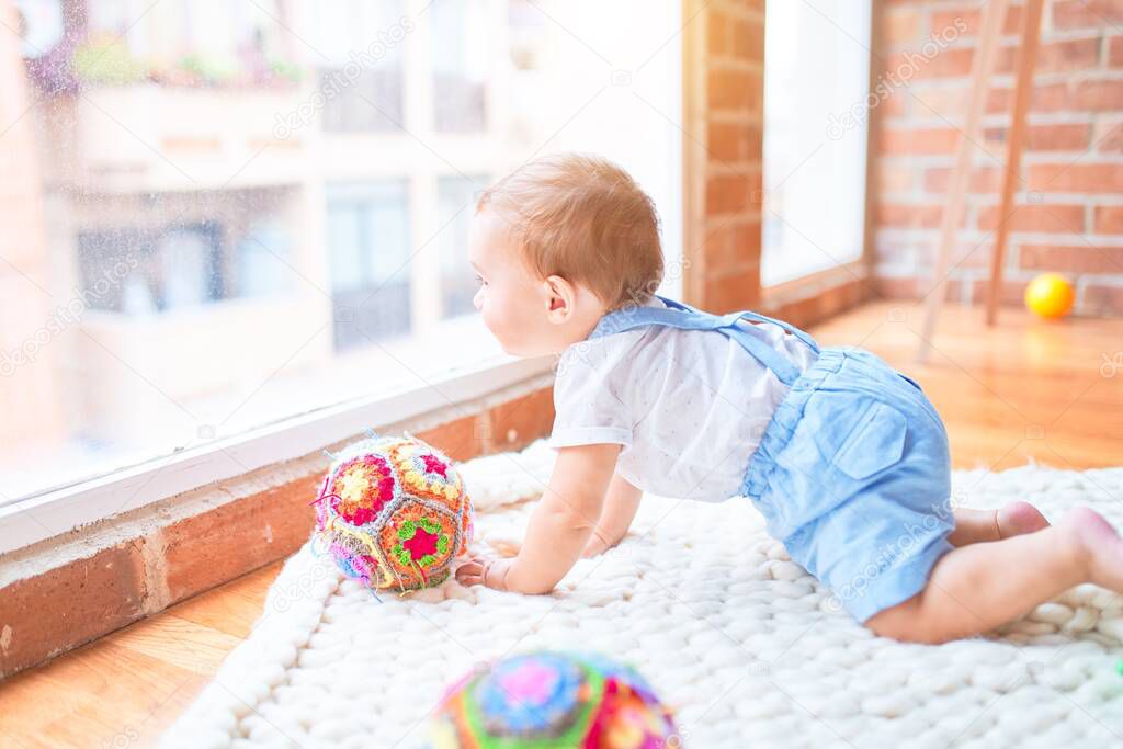Beautiful toddler crawling on the blanket looking through the window at kindergarten