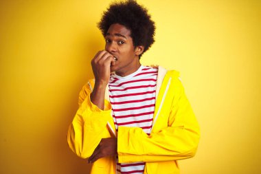 Siyah saçlı Afrikalı bir adam izole edilmiş sarı arka plan üzerinde duruyor. Ağzı tırnak yiyen elleri yüzünden gergin ve stresli görünüyor. Endişe sorunu.