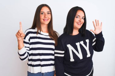 İzole edilmiş beyaz arka plan üzerinde duran gündelik giysiler giyen genç ve güzel kadınlar altı numaralı parmaklarıyla işaret ederken kendinden emin ve mutlu bir şekilde gülümsüyorlar..