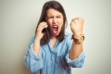 Genç ve güzel bir kadın, izole edilmiş arka planda akıllı telefon kullanarak konuşuyor. Sinirli ve sinirli bir şekilde bağırıyor, çıldırıyor ve el kaldırarak bağırıyor.