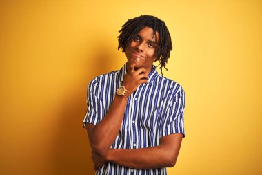 Rastgele çizgili tişört giyen Afro bir adam izole edilmiş sarı arka plan üzerinde kameraya güvenle bakıyor kollarını kavuşturmuş ve çenesini kaldırmış gülümsüyor. Olumlu düşünüyorum..