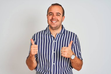 Mavi çizgili tişört giyen genç adam izole edilmiş beyaz arka plan işareti üzerinde duruyor. Elleriyle olumlu bir hareket yapıyor. Gülümsüyor ve mutlu. Neşeli ifade ve kazanan jest.