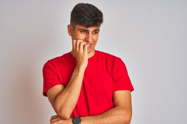İzole edilmiş beyaz arka plan üzerinde duran kırmızı tişörtlü genç Hintli adam elleri ağız yiyen tırnaklarla gergin ve stresli görünüyor. Endişe sorunu.